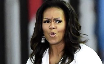Michelle Obama with pursed lips and furrowed brow, wearing a white shirt and dangling