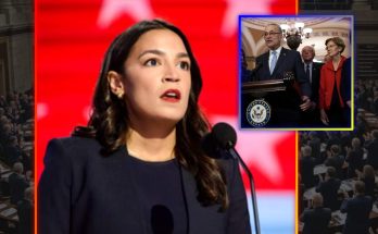 A woman speaking at a podium in a large chamber with people seated in rows behind her