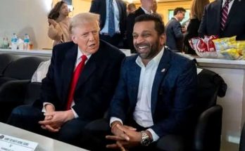 Donald Trump in a dark suit with red tie sits next to a man in a navy blazer and white