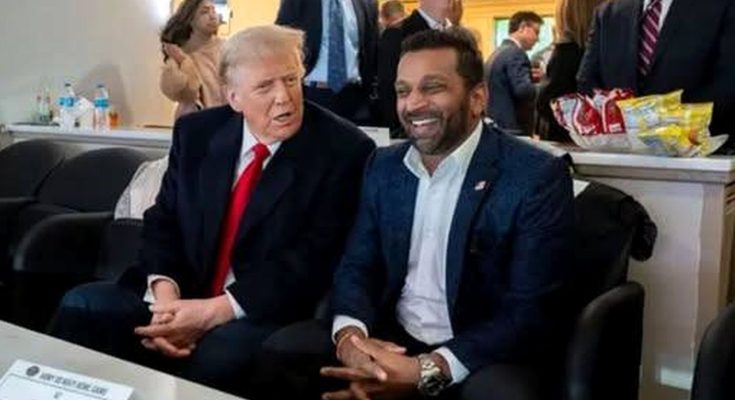 Donald Trump in a dark suit with red tie sits next to a man in a navy blazer and white