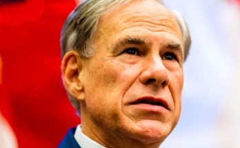 Close-up of a man with gray hair wearing a blue suit jacket and white collared shirt