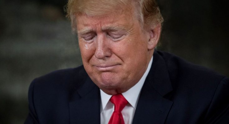 Donald Trump with eyes closed and a tear on his cheek, wearing a dark suit and red tie