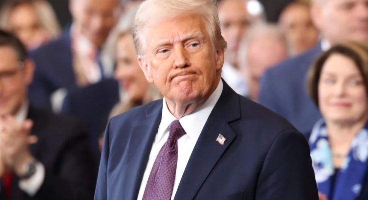 Donald Trump in a dark suit and red tie standing before a blurred crowd, with text above