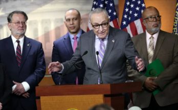 Chuck Schumer speaking at a podium with four other people standing behind him, American