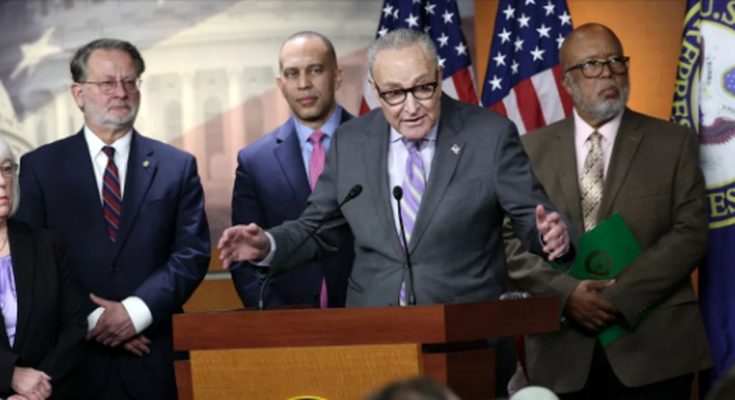 Chuck Schumer speaking at a podium with four other people standing behind him, American