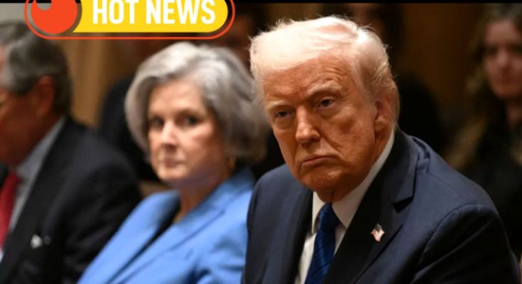 Donald Trump seated in a formal setting with a serious expression, wearing a dark suit