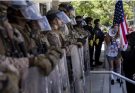A line of law enforcement officers in riot gear with shields faces a woman holding a