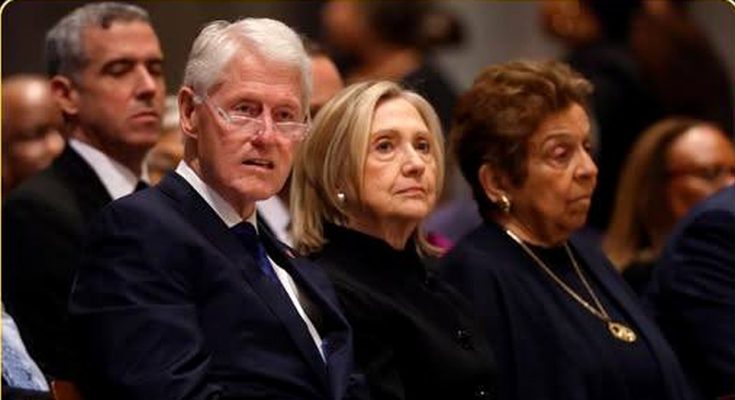 Bill Clinton and Hillary Clinton seated together at a formal event, both wearing dark