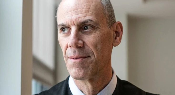 A bald man with gray hair on the sides wearing a black judicial robe with a white collar