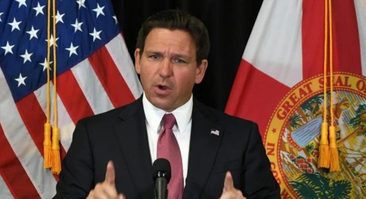 Ron DeSantis speaking at a podium with American and Florida state flags behind him, with