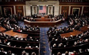 Interior view of a large legislative chamber with many people seated in rows, an