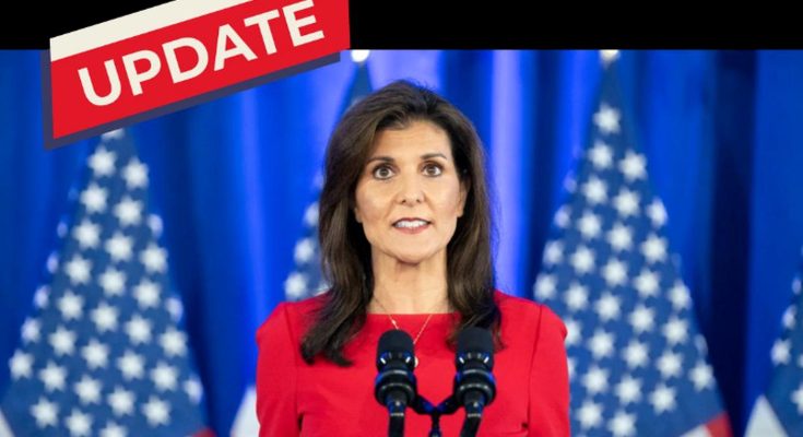 Nikki Haley in a red dress standing at a podium with two microphones, American flags