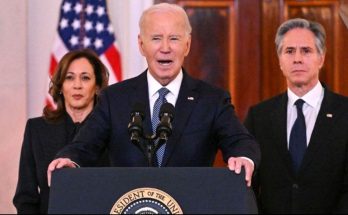 Joe Biden speaking at a podium with Kamala Harris and Antony Blinken standing behind