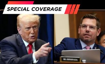 Two men in suits, one pointing forward, the other seated at a desk with a laptop