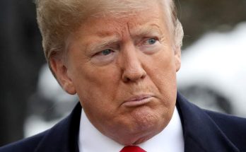 Close-up portrait of Donald Trump wearing a dark suit, white shirt, and red tie, with