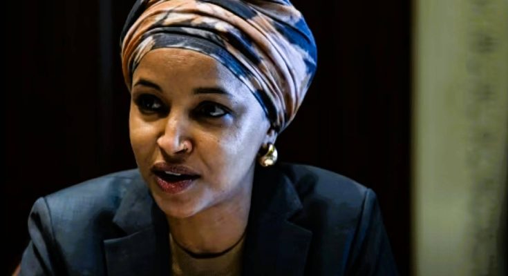 A woman wearing a striped turban and dark blazer speaks while looking to her right