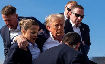 Donald Trump surrounded by Secret Service agents, one with an arm around a female agent