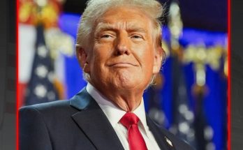 Donald Trump wearing a dark suit, white shirt, and red tie, with American flags visible