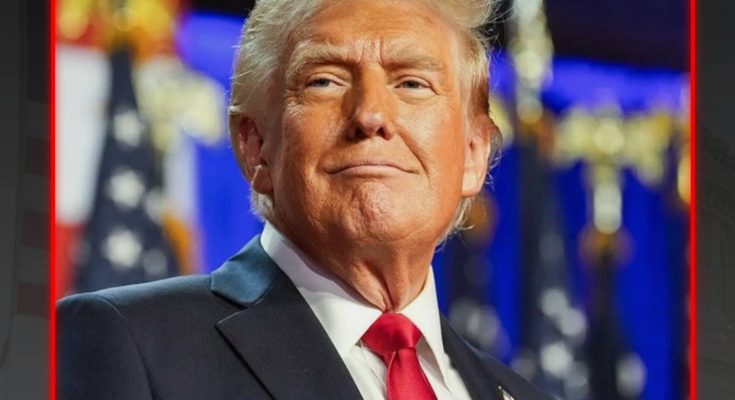 Donald Trump wearing a dark suit, white shirt, and red tie, with American flags visible