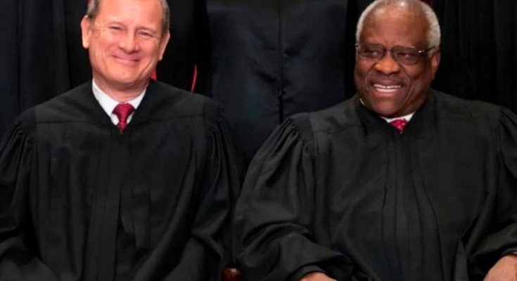 Two men in black judicial robes with red ties seated side by side, one with gray hair