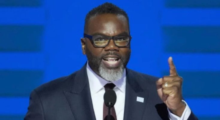 A man with a gray beard and glasses wearing a dark suit and tie speaks at a podium
