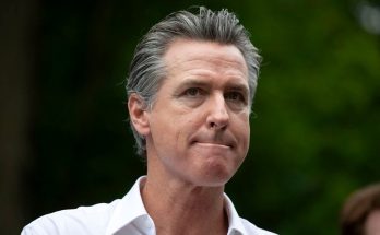 Gavin Newsom wearing a white collared shirt with gray hair, looking to the side with a
