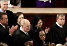 Several U.S. Supreme Court justices in black robes seated and clapping, including John