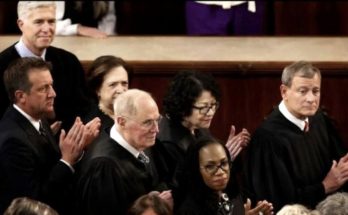 Several U.S. Supreme Court justices in black robes seated and clapping, including John