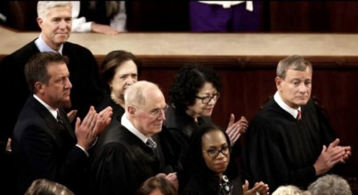 Several U.S. Supreme Court justices in black robes seated and clapping, including John