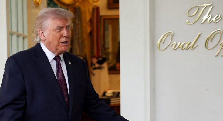Donald Trump standing in a doorway with arms extended, wearing a dark suit and red tie