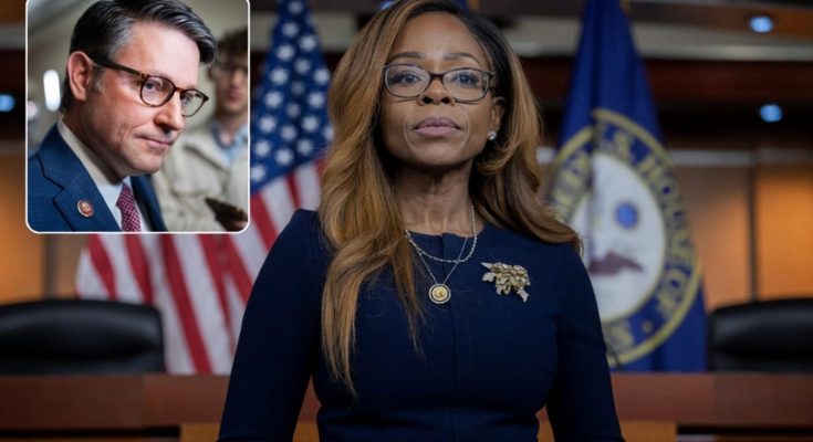 A woman with long brown hair wearing glasses and a dark blue dress stands in front of
