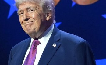 Donald Trump smiling while wearing a dark blue suit, white shirt, and purple patterned