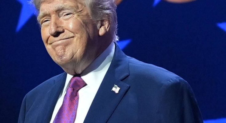 Donald Trump smiling while wearing a dark blue suit, white shirt, and purple patterned