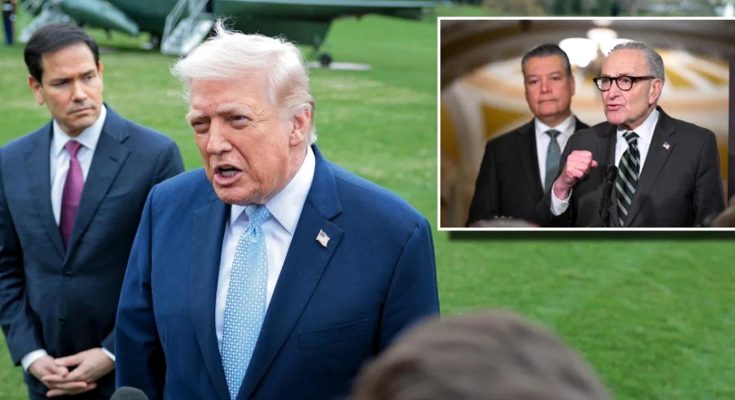 Donald Trump in a dark suit and red tie standing at a podium with a microphone, with an