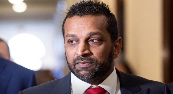 Kash Patel in dark suit with red tie, looking to his right in indoor hallway setting