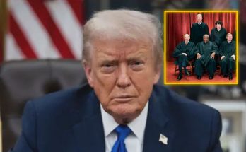 Donald Trump in a blue suit and tie sitting at a desk with an American flag behind him
