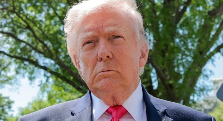 Donald Trump wearing a dark suit, white shirt, and red tie with an American flag pin
