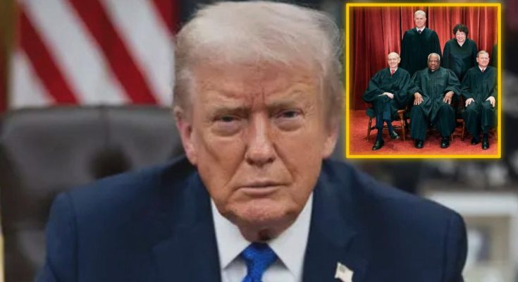 Donald Trump in a blue suit and tie sitting at a desk with an American flag behind him