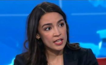 Alexandria Ocasio-Cortez speaking during a television interview with a blue background