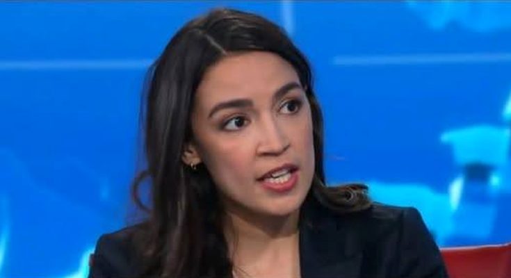 Alexandria Ocasio-Cortez speaking during a television interview with a blue background