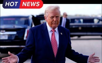 Donald Trump in a navy suit and red patterned tie stands with arms outstretched, palms