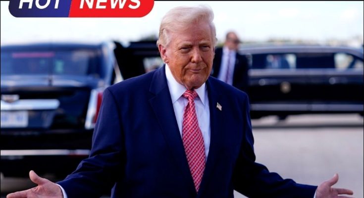 Donald Trump in a navy suit and red patterned tie stands with arms outstretched, palms