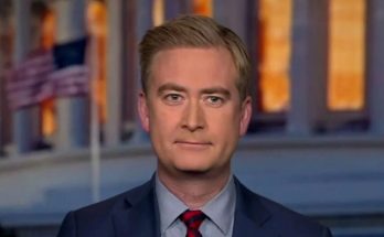 A man with light brown hair wearing a dark blue suit, light blue shirt, and red striped