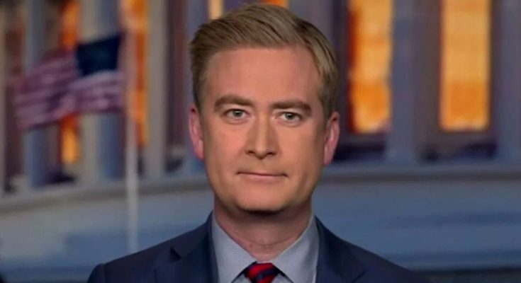 A man with light brown hair wearing a dark blue suit, light blue shirt, and red striped