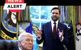 A man in a dark suit with a red tie stands gesturing with both hands while another man