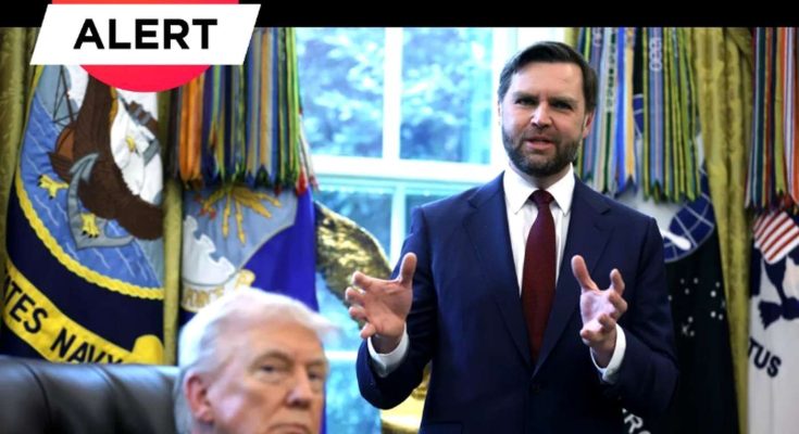 A man in a dark suit with a red tie stands gesturing with both hands while another man