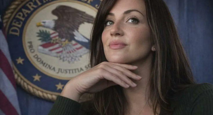 A woman with long brown hair wearing a green sweater and cross necklace rests her chin