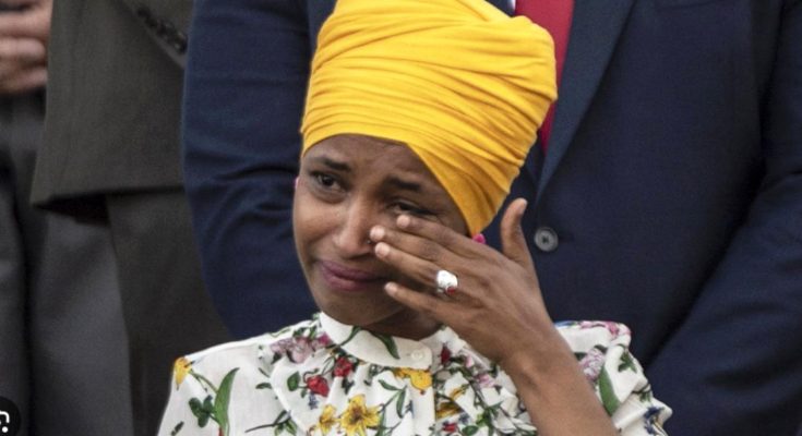 ilhan Omar wearing yellow turban and floral blouse wipes away tears with ringed hand