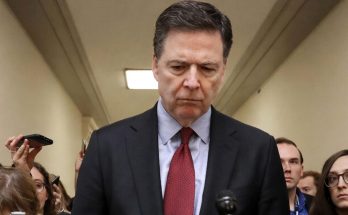 serious man in suit surrounded by reporters in a hallway