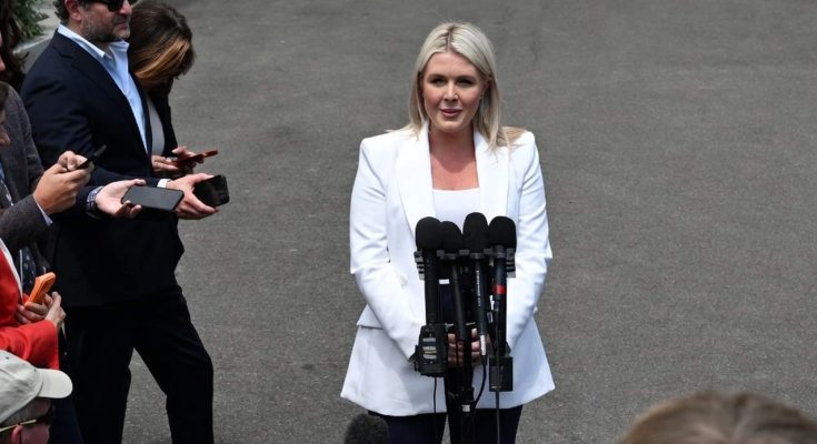 woman in white blazer speaks to media with microphones outdoors